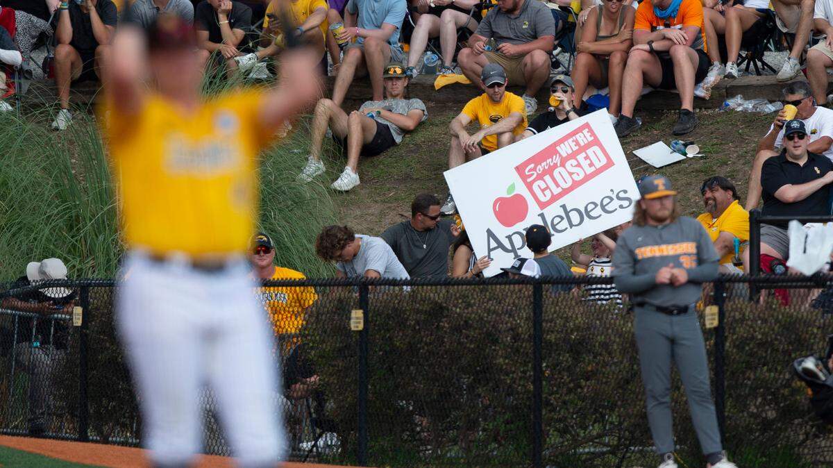 A fan holds a sign referencing the Applebee’s restaurant chain during NCAA Super Regionals at Pete Taylor Park in Hattiesburg on Sunday, June 11, 2023.