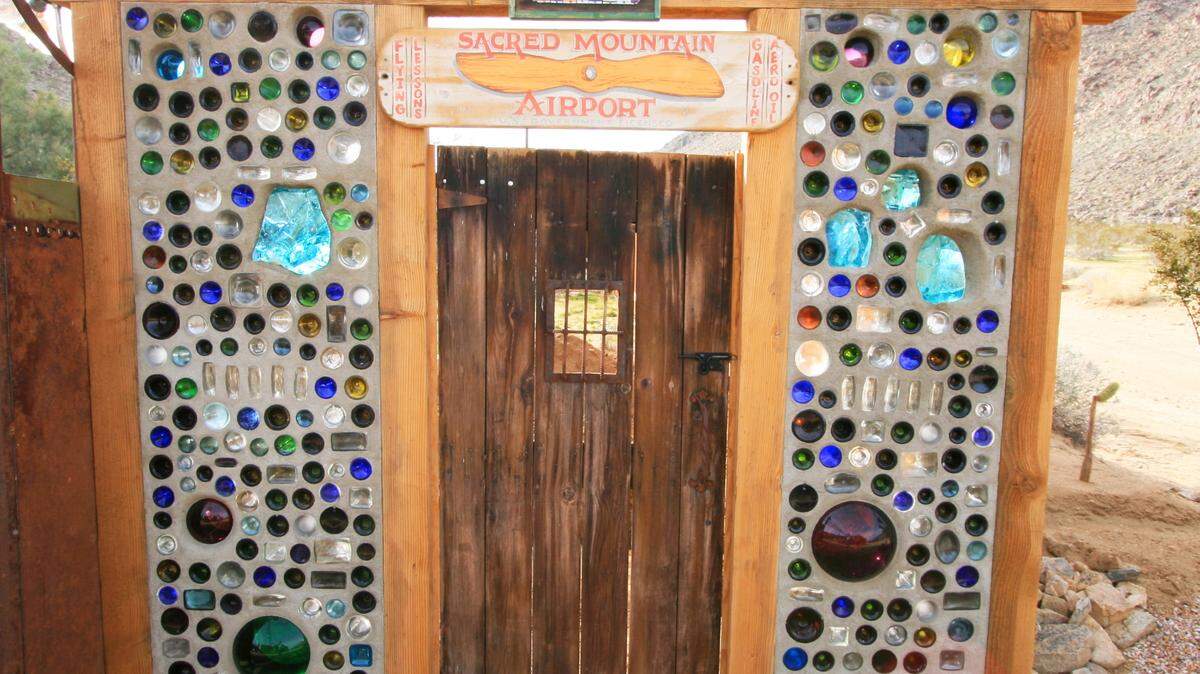TNSThe essence of a rustic entry gate is flanked by mixed bottle walls featuring slag glass and a variety of colors.
