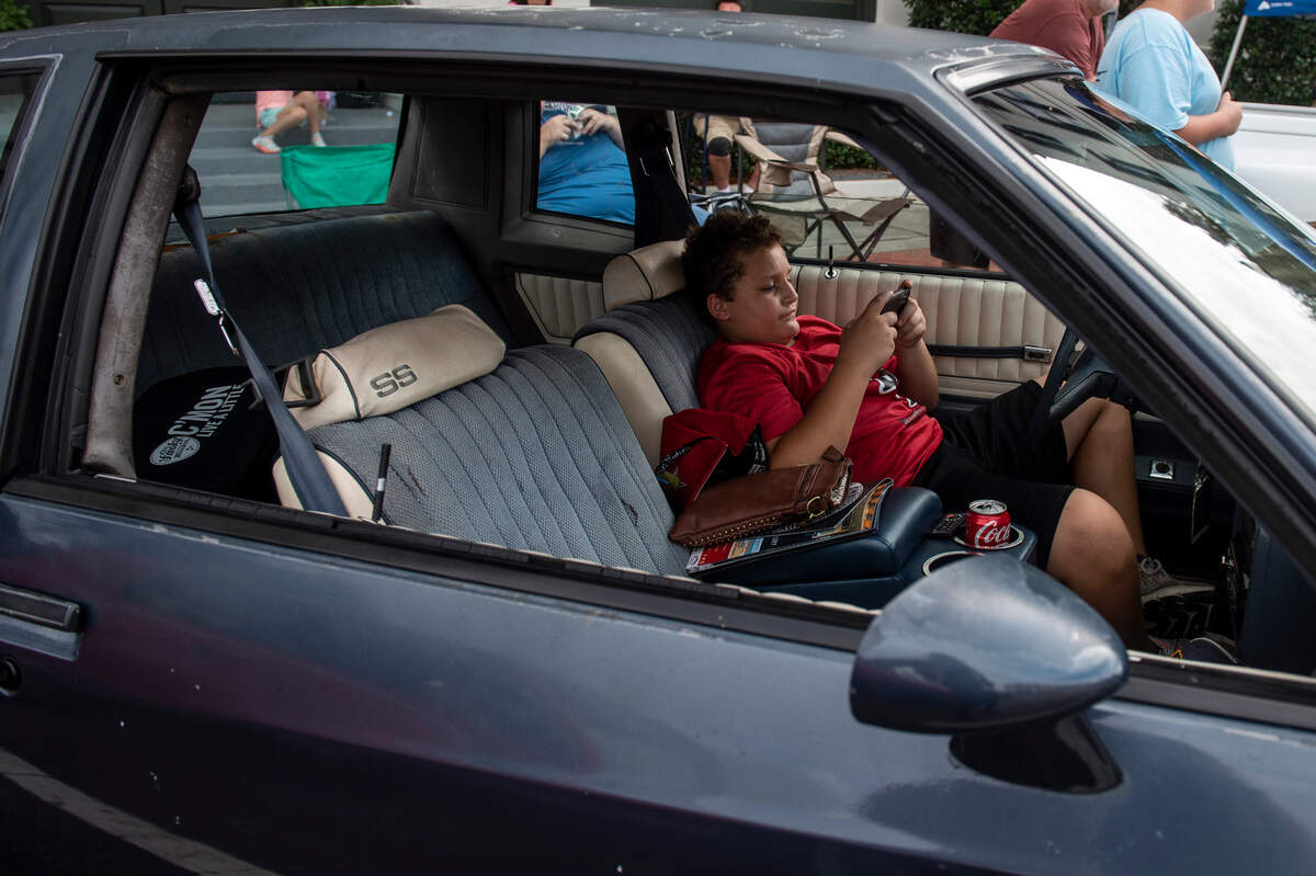 Conner Huguet, 12, plays games on his phone as he sits inside his aunt’s 1983 Monte Carlo during View the Cruise on Sunday, Oct. 3, 2021.