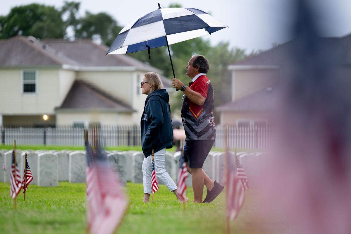 Event attendees walk through a field with tombstones and American flags after a ceremony at Biloxi National Cemetery on Monday, May 25, 2026.