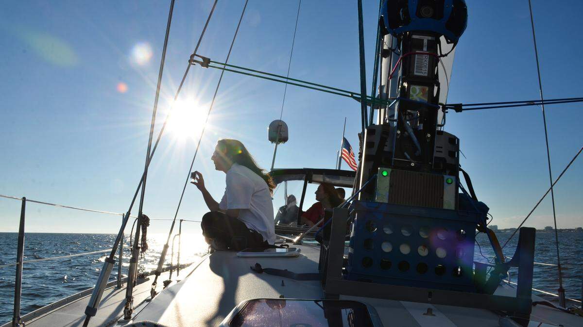 JUSTIN MITCHELL/SUN HERALDKelsey King, left, takes a photo of dolphins playing in the Mississippi Sound during a sail on North Star Charters to collect content for Google Trekker. The machine, right, provides 360-views of areas that can't be captured from a vehicle.