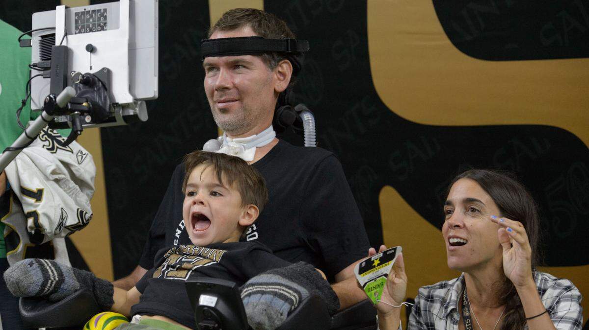 Former New Orleans Saints player Steve Gleason watches the boat race as his son, Rivers, moves his arms inside gloves next to Gleason’s wife, Michel Gleason, at a preseason game. The Gleasons are expecting a second child in October.