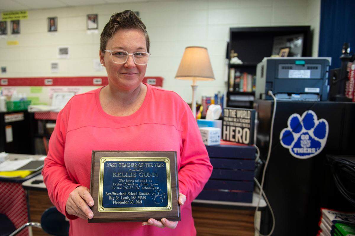 U.S. History teacher Kellie Zimmerman Gunn proudly holds up her teacher of the year plaque in her class room at Bay High School in Bay St. Louis on Tuesday, March 22, 2022. Gunn has regularly had to clean mold off the walls of her classroom, due to the high humidity in the room.