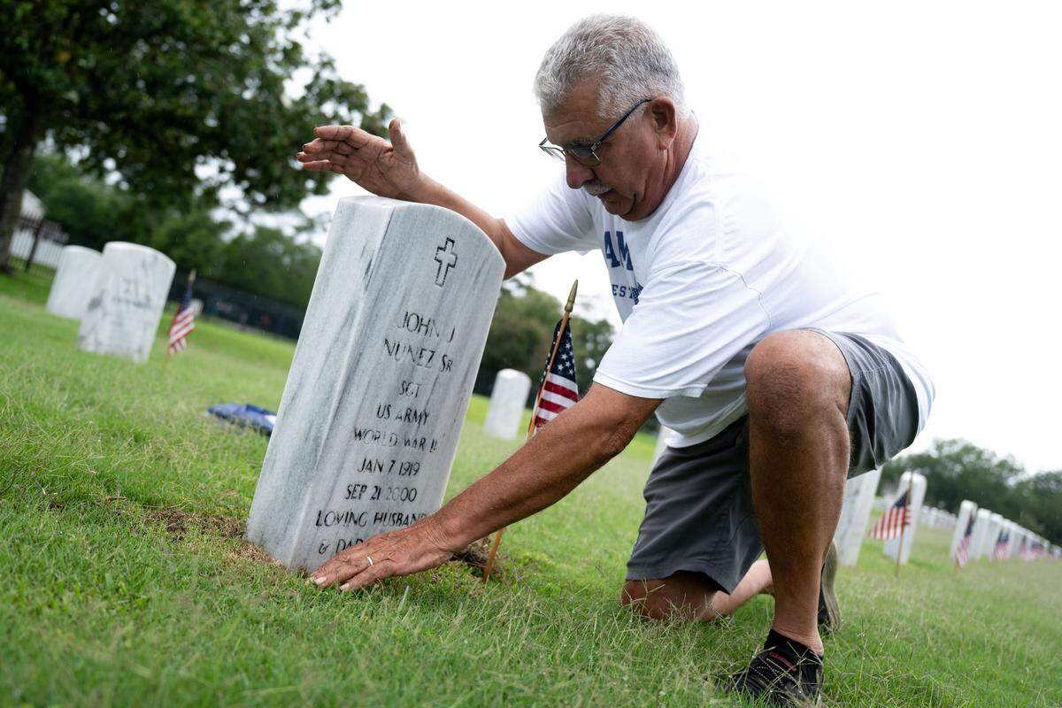 Brian Nunez clears out overgrown grass from his parent’s tombstone during a ceremony at Biloxi National Cemetery on Monday, May 25, 2026.