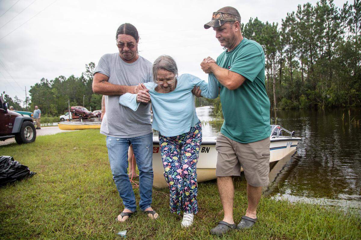 Stanley Delle, left, and Jeff Delle help 81-year-old Eileen Delle onto dry land Monday, Aug. 30, 2021 after floodwaters from Hurricane Ida surrounded her elevated home in the Shoreline Park community in Bay St. Louis.