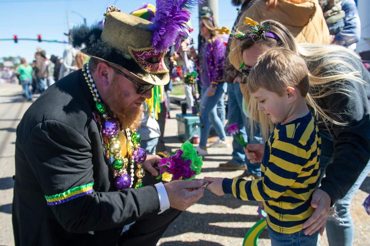 A member of the Ole Biloxi Marching Club hands flowers to parade watchers during the Krewe of Nereids Mardi Gras parade on Highway 90 in Bay St. Louis on Sunday, Feb. 12, 2023.