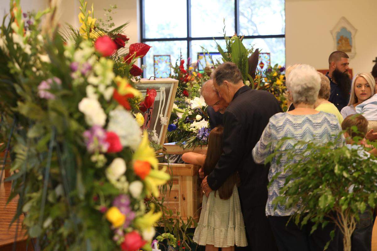Anistyn Hoda, 8, views stepfather Cayce Seal’s body at his funeral service at St. Clare Catholic Church on July 1, 2021. Cayce’s father, Doug Seal, and uncle, Buddy Seal embrace the girl.
