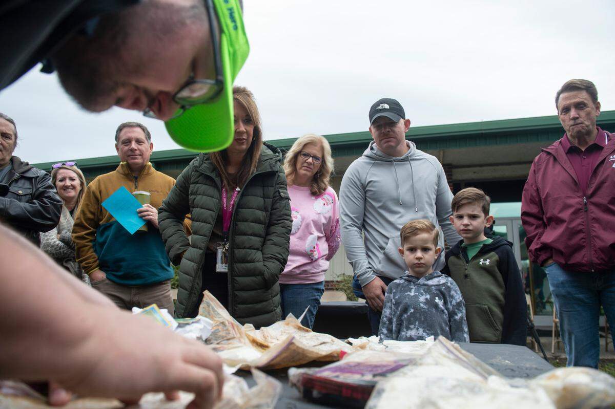 Families and staff look on as Colby Holland, center, a former student at W. J. Quarles Elementary in Long Beach, sorts through items from a time capsule on Friday, Dec. 13, 2024, that he and his classmates buried in 1999.
