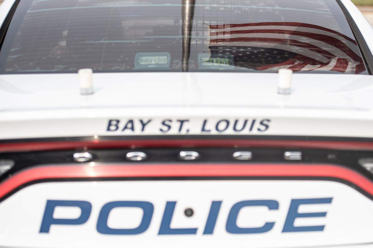 The American flag flies at half staff over a police car with a thin blue line flag outside the Bay St. Louis Police Station in honor of officers Steven Robin and Brandon Estorffe who were killed in the line of duty on Wednesday, Dec. 14, 2022.