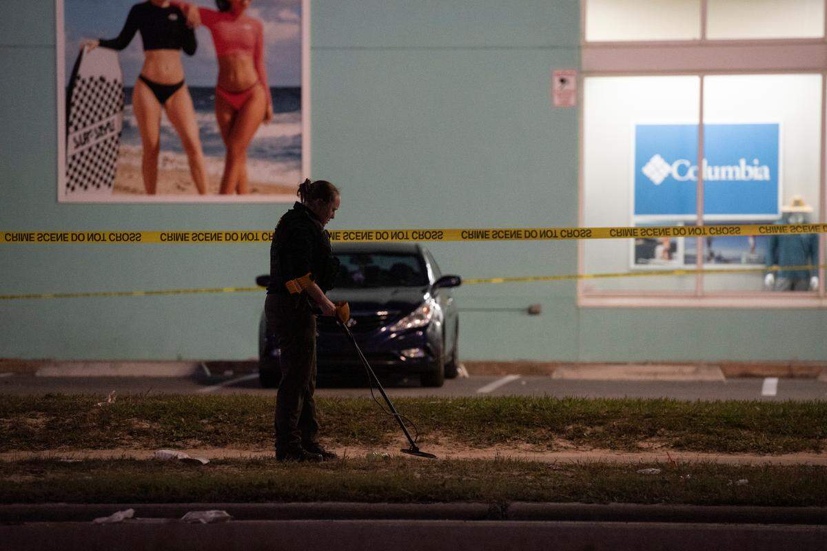 A law enforcement officer uses a metal detector on the ground to look for evidence outside Surf Style in Biloxi after a chaotic shooting during Black Spring Break that left one police officer injured on Sunday, April 16, 2023.