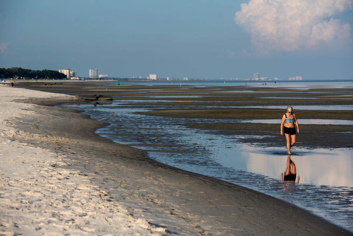 Present: The reflection of a person beach walking is seen in the water on the Gulfport beach.