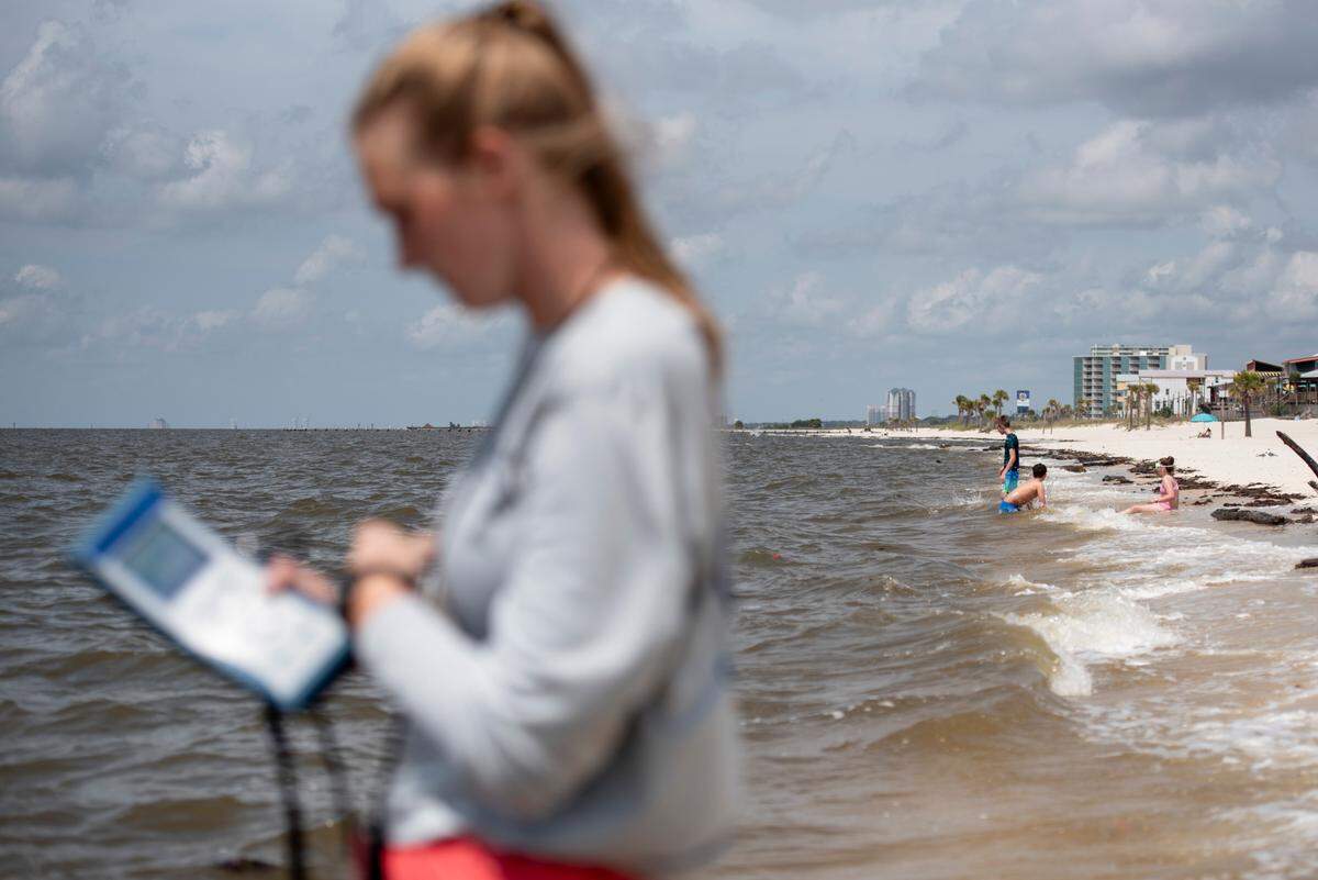 Children play at the beach as Jennifer Ahlbrand, an environmental natural resource specialist with the Mississippi Department of Environmental Quality, collects a water sample to test for enterococcus on Wednesday, April 30, 2025. If water from a beach tests positive for enterococcus, the public will be warned not to swim in the water.