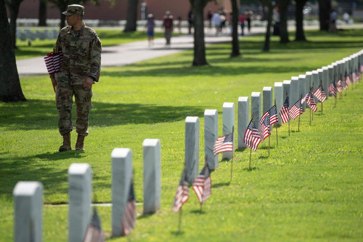A member of the Air Force walks among the graves after helping to place thousands of tiny American flags on the graves of American service members at Biloxi National Cemetery in Biloxi ahead of Memorial Day on Saturday, May 25, 2024.