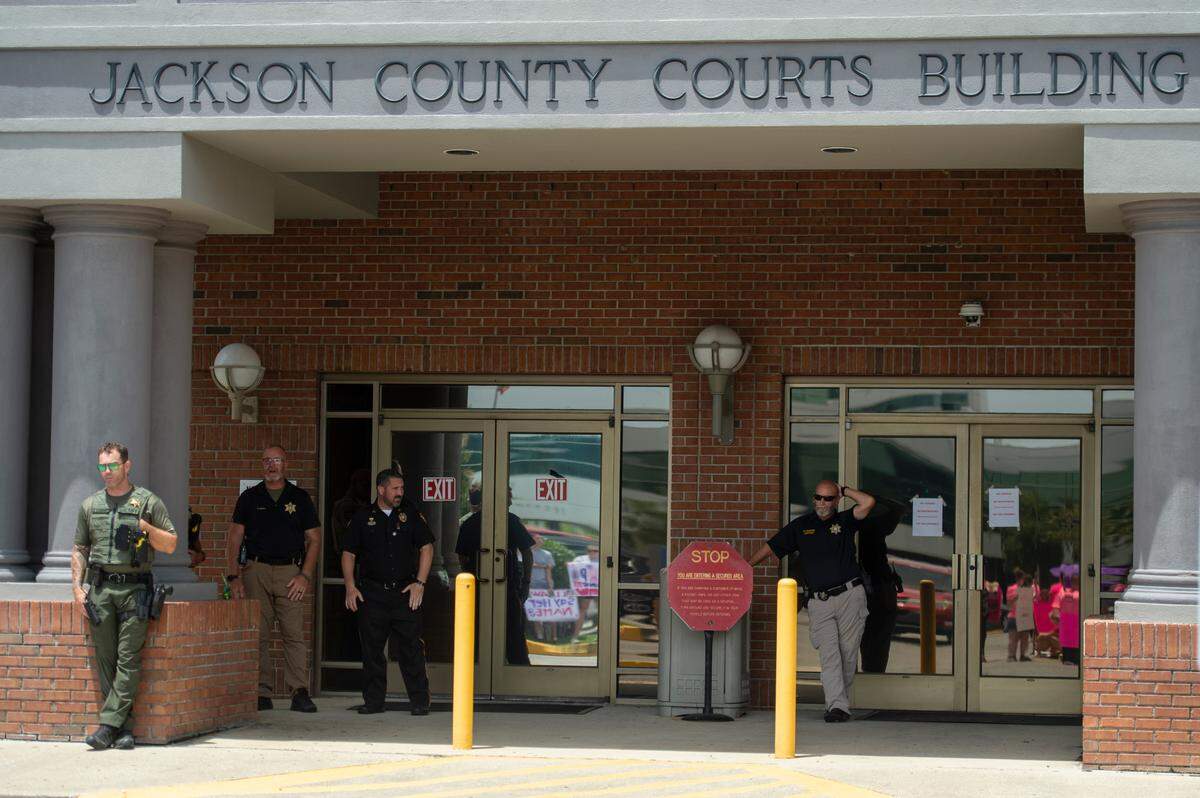 Members of law enforcement watch protestors from outside the Jackson County Courts building as a hearing in a chancery court case involving Heather Wyatt takes place inside on Thursday, July 18, 2024.