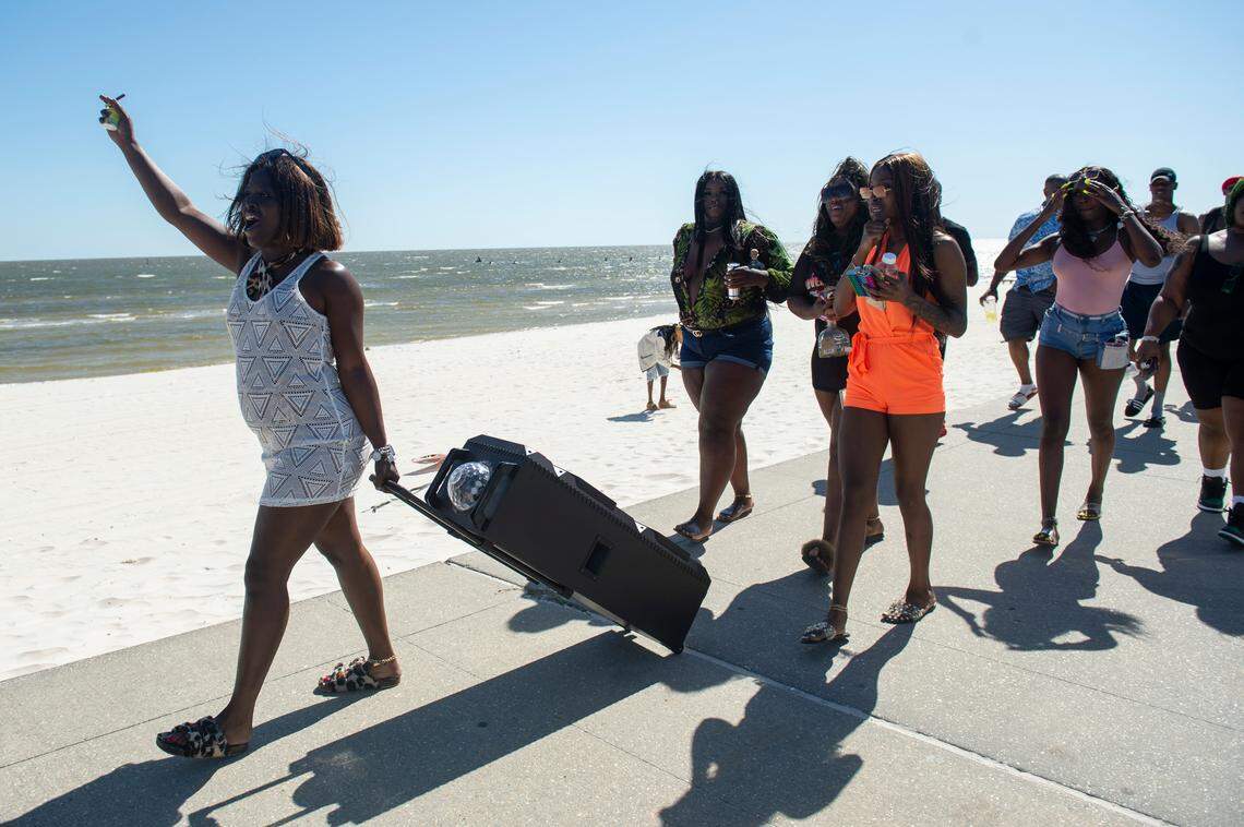Spring breakers walk down the beach playing music on large speakers during Black Spring Break in Biloxi on Saturday, April 9, 2022.