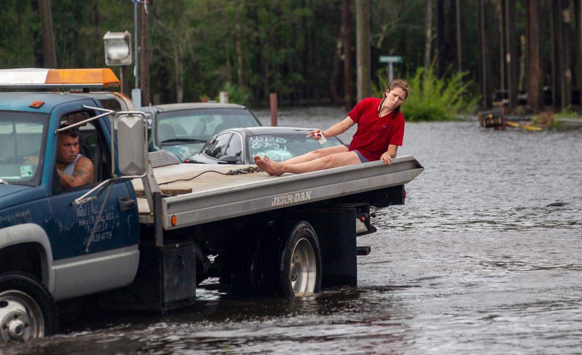 A woman rides on the back of a tow truck through floodwaters Monday, Aug. 30, 2021 in Shoreline Park community in Bay St. Louis.