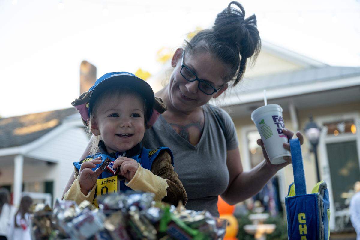 Maeveh Hudgens smiles as she picks up candy while being held by Heather Klein during Boo On The Rue in Biloxi on Thursday, October 30, 2025.