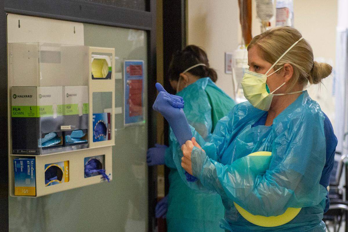 A nurse puts on protective equipment including gloves in preparation to flip a COVID-19 patient inside the ICU at Singing River Health System hospital in Ocean Springs on Tuesday, July 27, 2021.