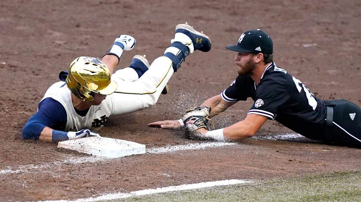 Notre Dame’s Brooks Coetzee (42) safely tags first base as Mississippi State’s Luke Hancock (20) dives towards him after retrieving a passed ball during the NCAA college baseball super regional game, Sunday, June 13, 2021, in Starkville, Miss. (AP Photo/Rogelio V. Solis)
