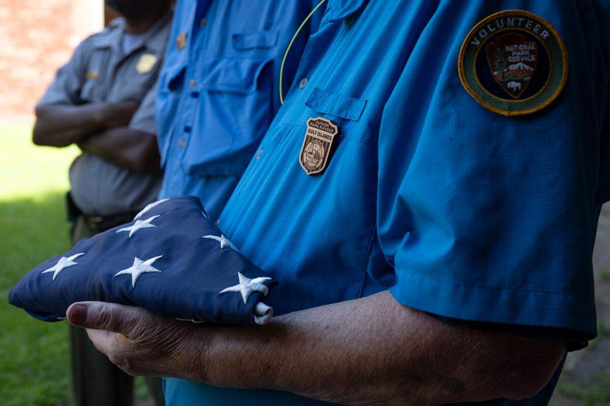A volunteer holds a folded American flag — a gift for 100 year old volunteer Jack Madison — during Madison’s final tour on Friday, July 11, 2025.
