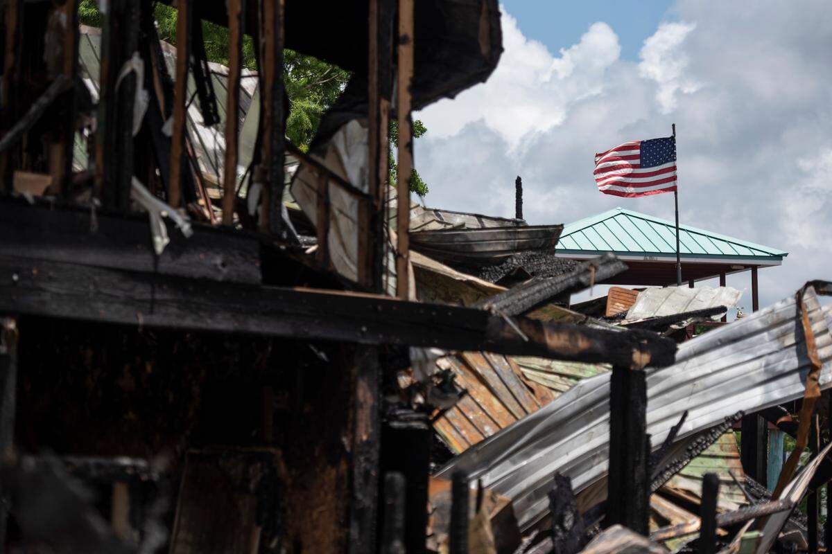 A flag from a neighboring house stands over the remains of two houses that caught fire on Saturday night on Tuesday, May 31, 2022.