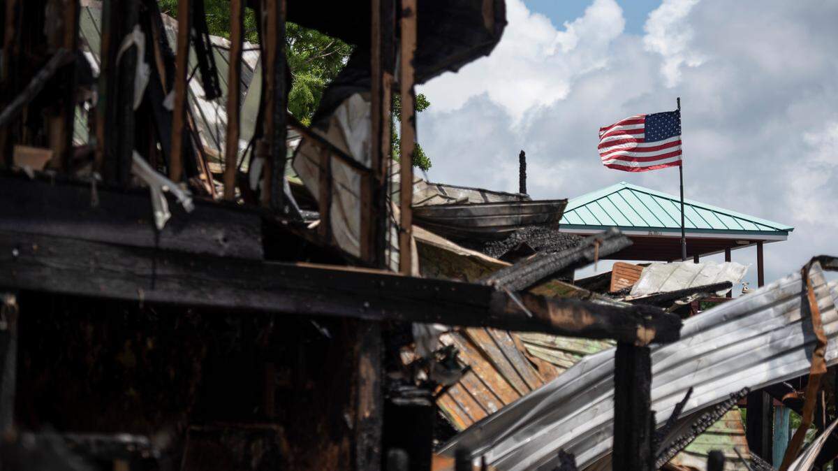 A flag from a neighboring house stands over the remains of two houses that caught fire on Saturday night on Tuesday, May 31, 2022.