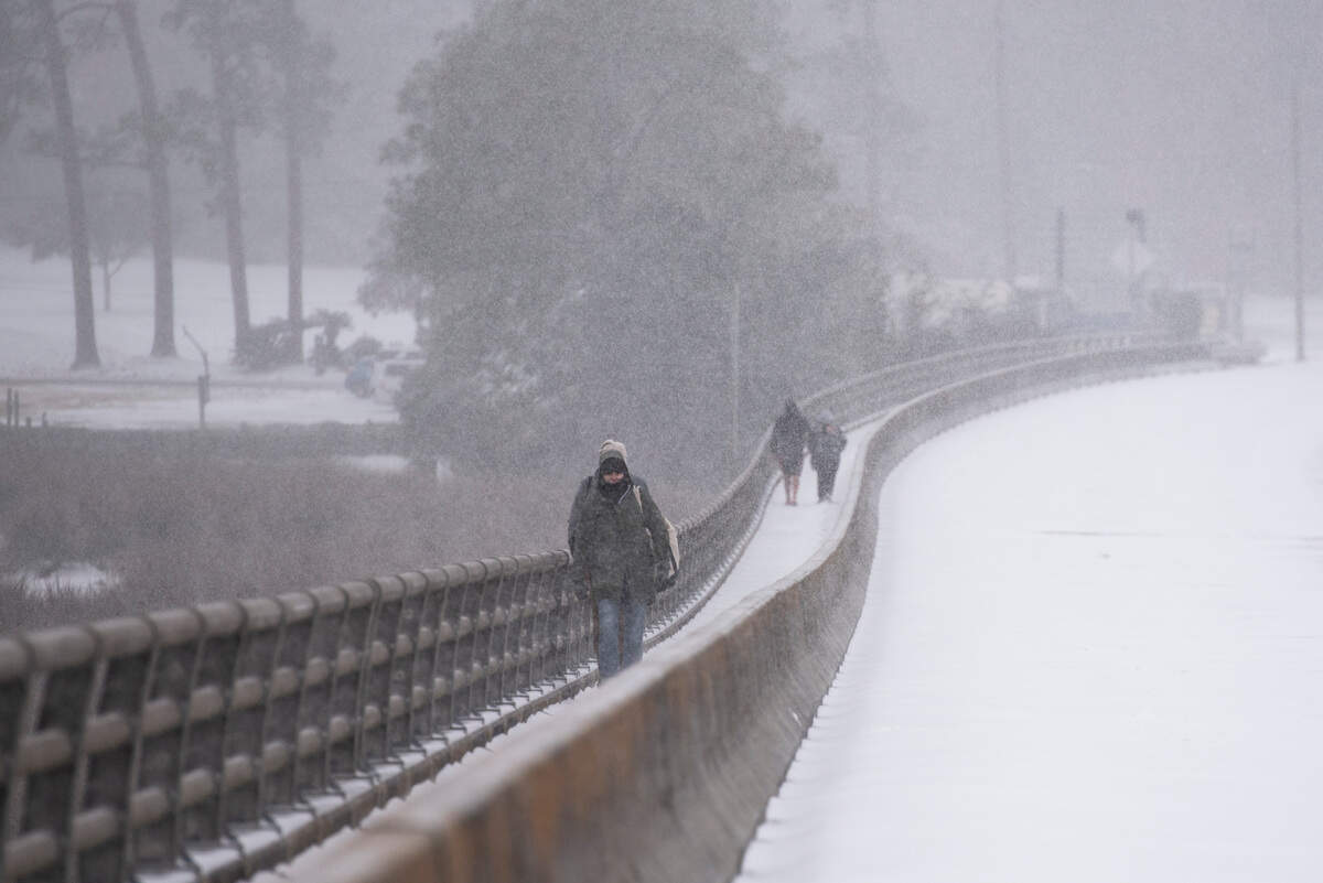 Pedestrians walk through the snow along the Fort Bayou Bridge during a winter storm on the Mississippi Coast on Tuesday, Jan. 21, 2025.