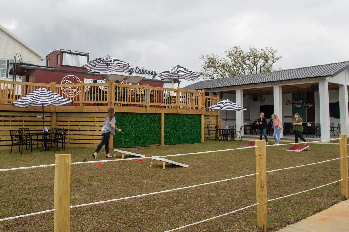 Customers play corn hole on the lawn of The Juicy Caboosy, a juice bar and restaurant built into a vintage train caboose, in Long Beach on Thursday, March 2, 2023.