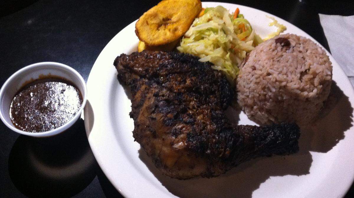 NATE THURMAN/SUN HERALDAn order of jerk chicken with sides of rice and peas, steamed cabbage and fried plantains from Taste of Jamaica restaurant in Ocean Springs. On the left is a cup of zesty jerk sauce.