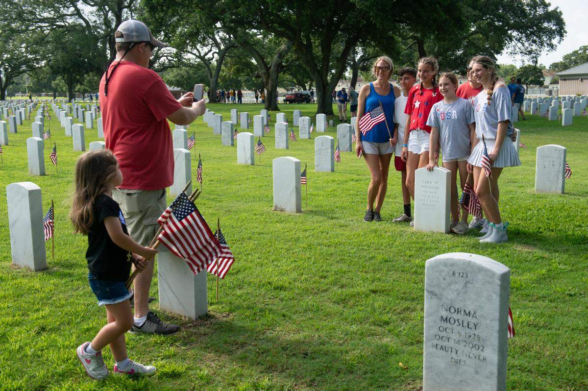 The Necaise family poses for a photo with the tombstone of their great grandparents as they help place American flags on the graves of American service members at Biloxi National Cemetery in Biloxi ahead of Memorial Day on Saturday, May 25, 2024.