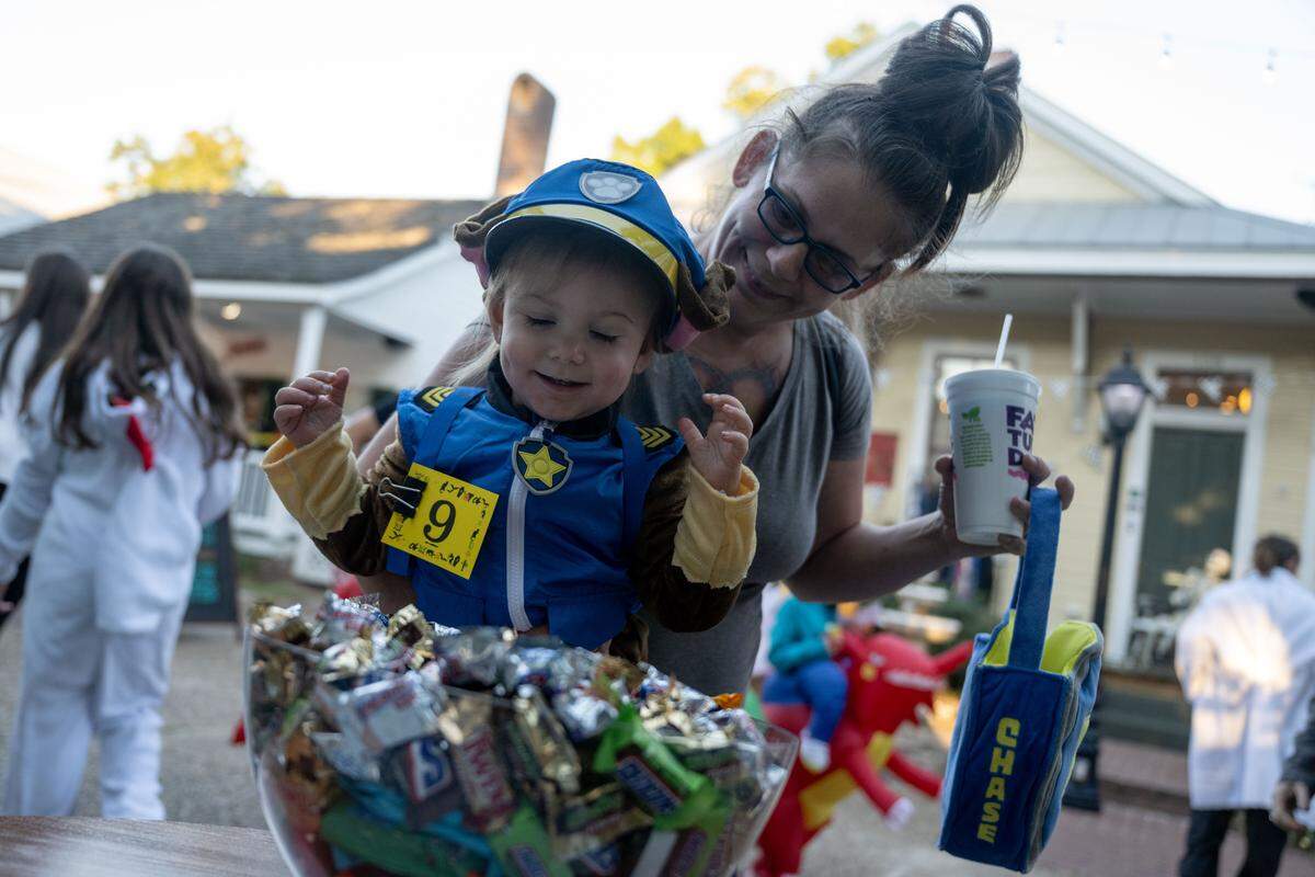Maeveh Hudgens reaches out to pick up candy while being held by Heather Klein during Boo On The Rue in Biloxi on Thursday, October 30, 2025.