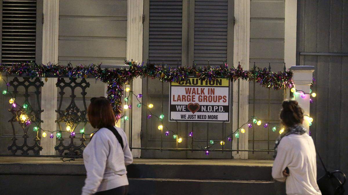 In this Jan. 18, 2015 photo, people walk past a sign encouraging people to walk in large groups, in the French Quarter of New Orleans. A spike in violent crime in the French Quarter is unsettling residents and comes just as New Orleans prepares to host crowds of tourists for Mardi Gras.