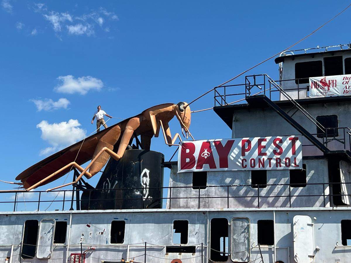 Bruno Milanese, owner of Bay Pest Control, stands on top of a steel cockroach on an old tugboat as the boat is moved from Biloxi Back Bay to the Schooner Pier. Milanese is sponsoring the creation as an artificial reef being sunk in the Gulf of Mexico.