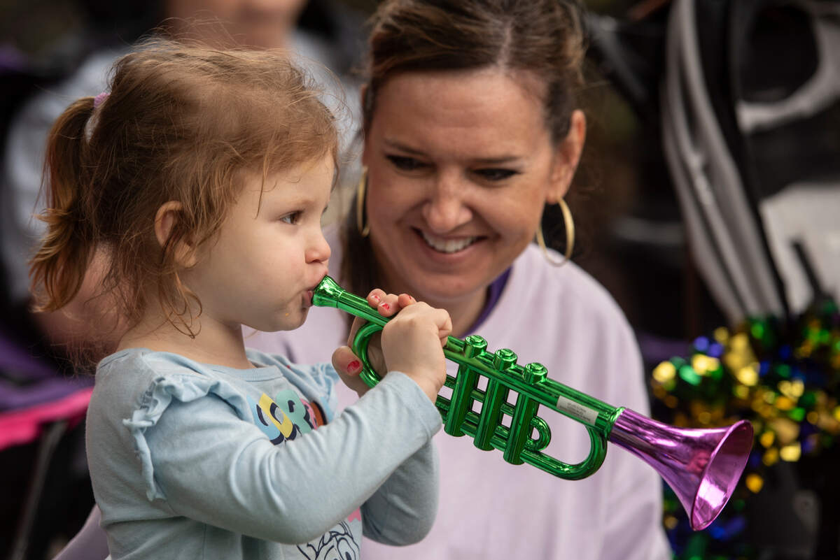 Miss Bufkin, of Laurel, watches as Oakleigh Reid, 2, plays with a pretend trumpet during The Ocean Springs Elks Carnival Parade in downtown Ocean Springs on Saturday, Jan. 27, 2024.