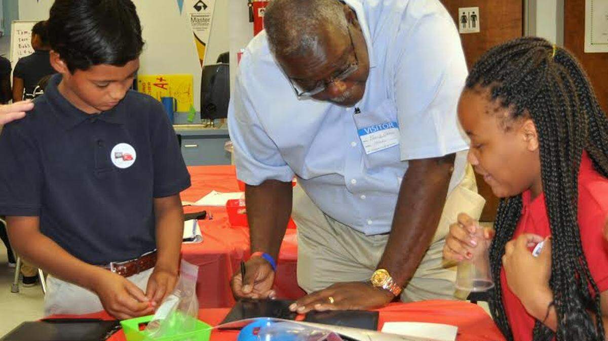 Singing River Academy students Andres Andino, left, and Ya'Shineek Williams, right, give Chevron Pascagoula Refinery General Manager Bruce Chinn some pointers on how to do a math problem on a Boogie Board. The technology was funded through Chevron's Fuel Your School program in partnership with a Donors Choose grant.