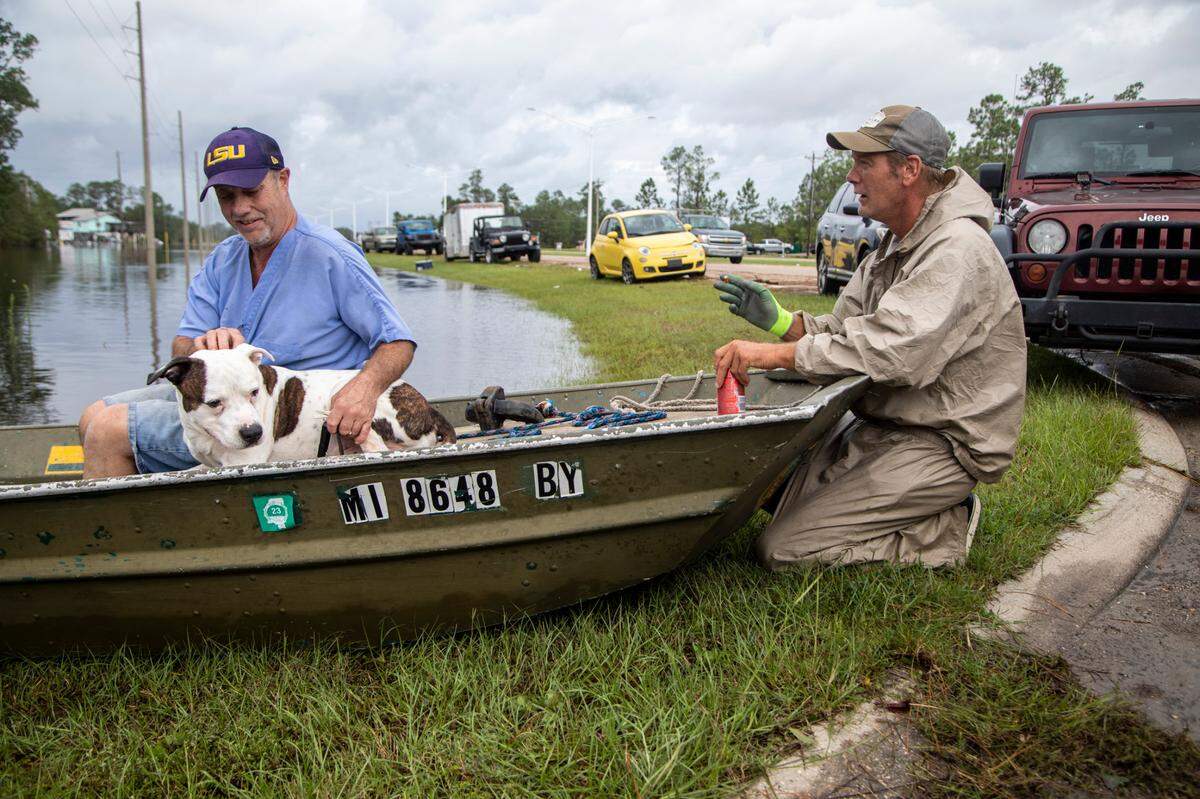 Eddie Gonzales, right prepares to ferry Lloyd Ernest and his dog “Cujo” through floodwaters back to their elevated home in the Shoreline Park community in Bay St. Louis Monday, Aug. 30, 2021.