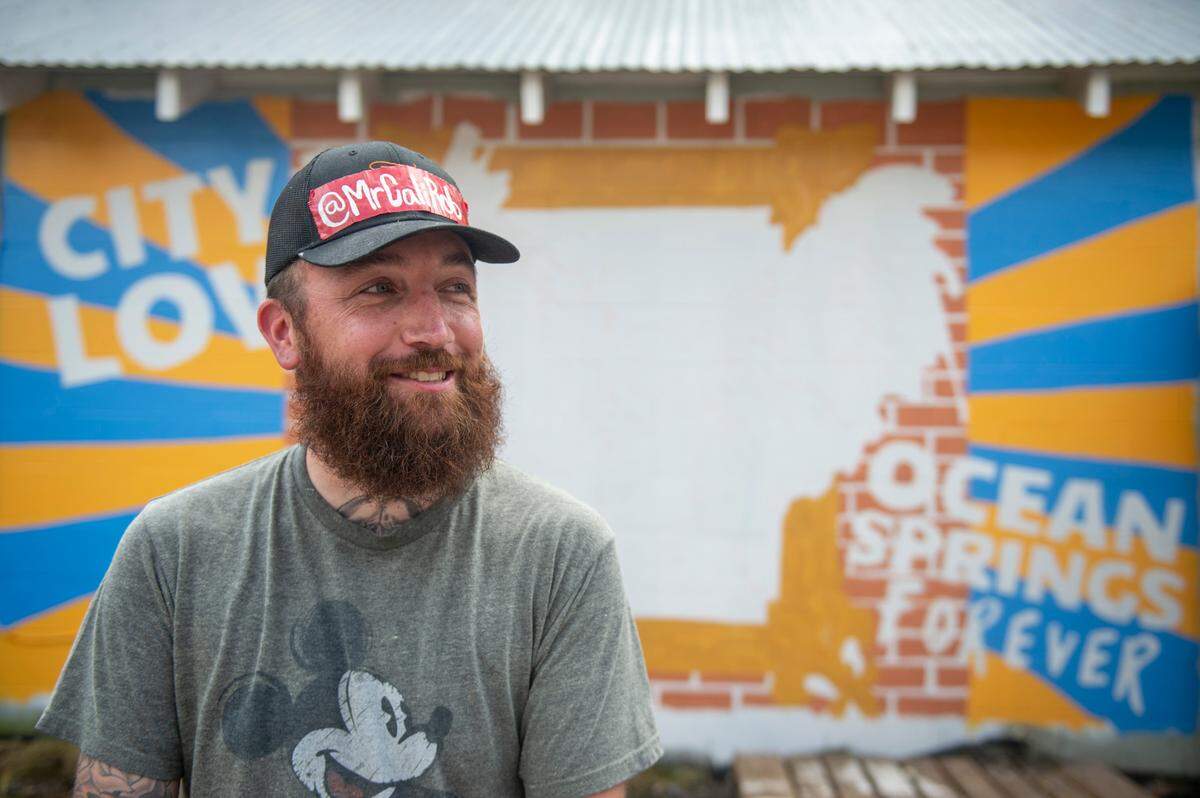 Mr. Cali Rob, a local artist from Ocean Springs, poses for a portrait in front of a mural he is painting in honor of Carl the rooster on the side of Lil’ Market in Ocean Springs on Monday, May 2, 2022.