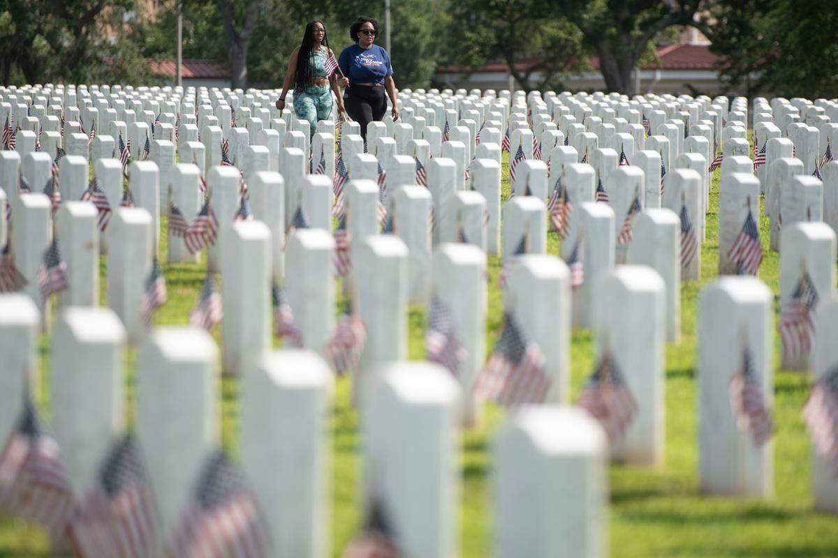 Volunteers walk among the graves after helping to place thousands of tiny American flags on the graves of American service members at Biloxi National Cemetery in Biloxi ahead of Memorial Day on Saturday, May 25, 2024.
