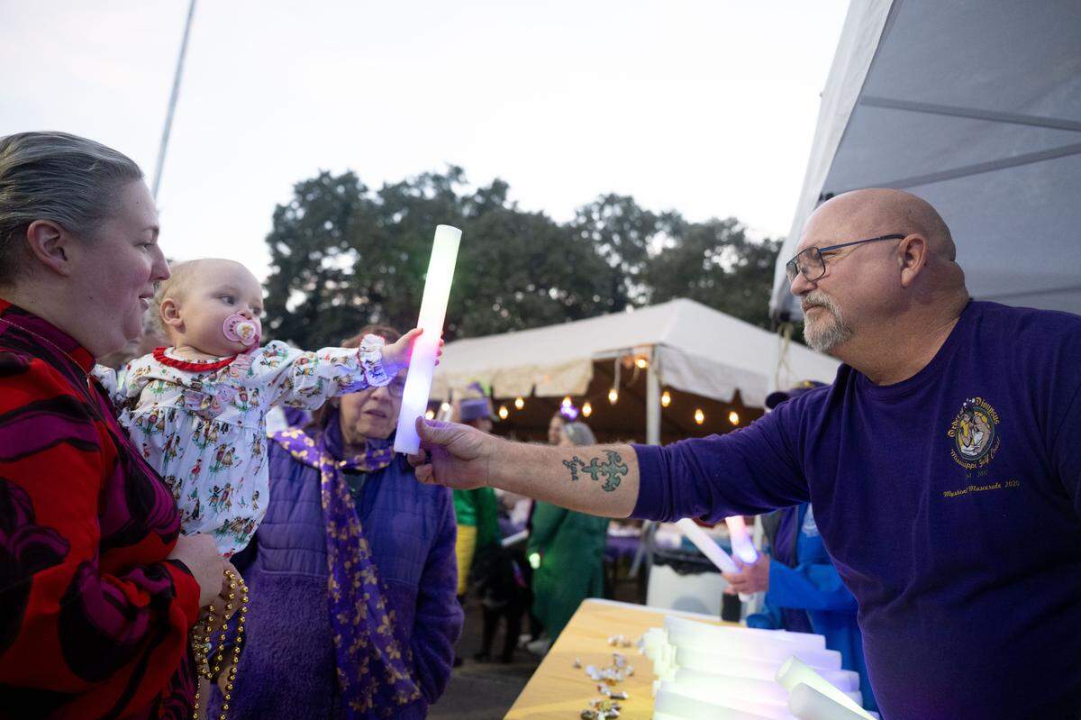 Daniel Joyner, right, hands out a light stick to Scarlett Greene and her daughter Mackenzie, left, during a 12th Night Celebration in Biloxi on Monday, Jan. 5, 2026.