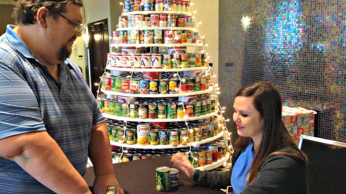 MARY PEREZ/SUN HERALD 
 A Christmas tree of food donations collected at Treasure Bay Casino will be donated to Biloxi's Back Bay Mission this week to help feed those in need over the holidays. Frank Kappler, left, a slot technician manager, brings a bag of canned goods for Sarah Loiacano, marketing coordinator, to add to the donations. The casino has done food drives in the past but this is the first time it was tied to a promotion -- the "$20,000 Because We Can Slot Tournament." Mike Rumore drove from Tampa, Fla., for the promotion that provided players club points for each can of food donated. He and others said although the points are nice, they wanted to give back to the community.