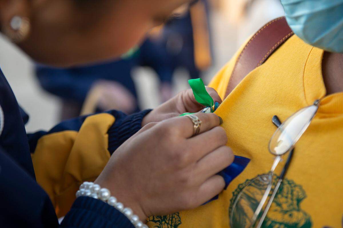 A cheerleader affixes a ribbon to a mourner’s shirt before a vigil for Gautier High School student Shermarion Miner at Gautier High School on Thursday, Jan. 16, 2025.