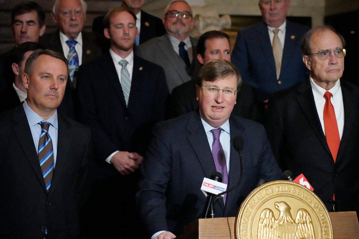 Mississippi Republican Gov. Tate Reeves, center, stands with House Speaker Jason White, R-West, left, and Republican Lt. Gov. Delbert Hosemann, right, as well as the legislators behind him, as he praises the passing of a state incentives package for a Mississippi factory that will manufacture batteries for electric vehicles.