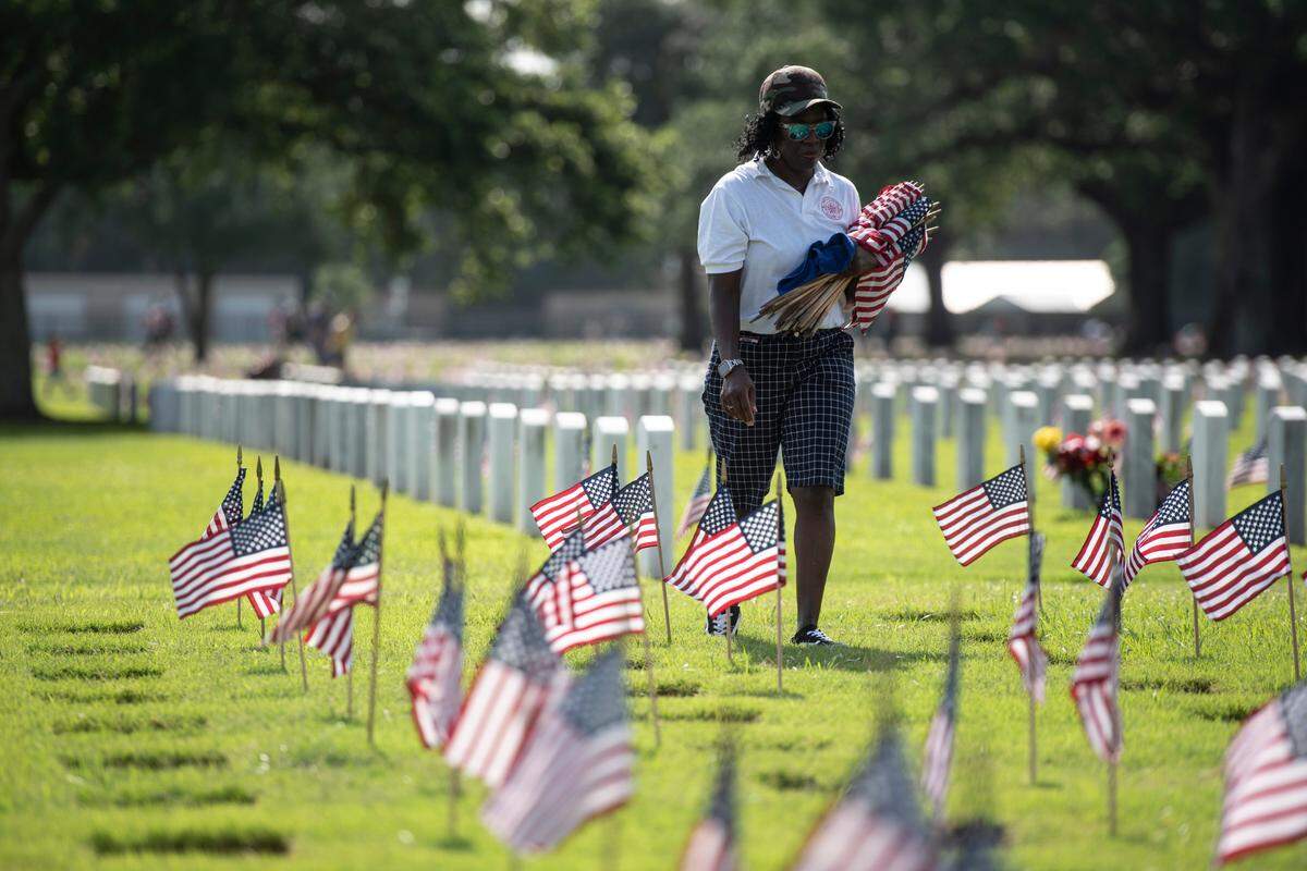 Volunteers help place thousands of tiny American flags on the graves of American service members at Biloxi National Cemetery in Biloxi ahead of Memorial Day on Saturday, May 25, 2024.