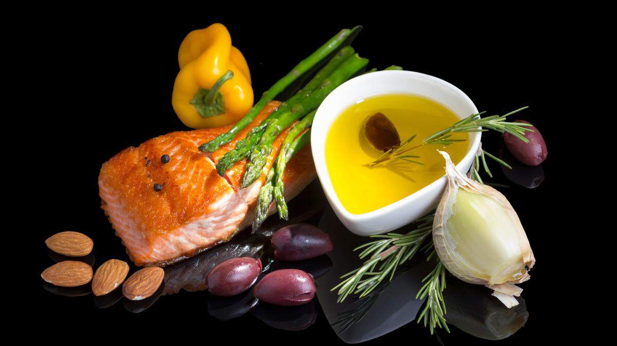 Mediterranean omega-3 diet. Fish steak, olives, nuts and herbs isolated on black background with reflection.