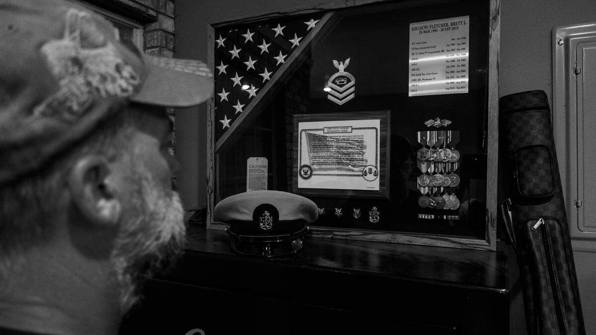 Brett looks at the shadow box above his Cabella cabinet, which holds an American flag and a litany of medals from his service overseas in the Navy.