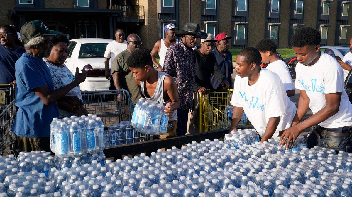 Residents of the Golden Keys Senior Living apartments flock to a trailer full of water being delivered by the AIDS Healthcare Foundation in Jackson, Miss., Thursday, Sept. 1, 2022. A recent flood worsened Jackson’s long standing water system problems. (AP Photo/Steve Helber)