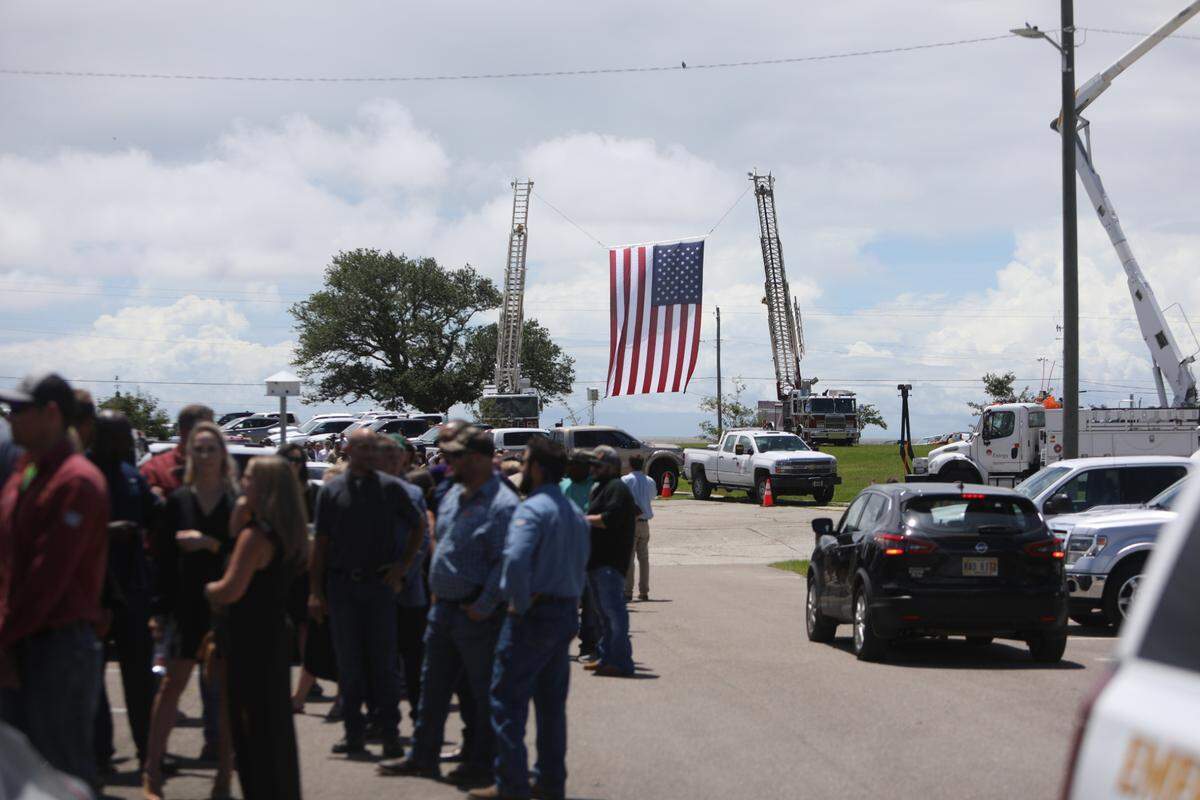 Hundreds wait outside St. Clare Catholic Church, including many linemen and first responders, to pay respects to lineman Cayce Seal on July 1, 2021. Entergy crews and Bay St. Louis firefighters raised three American flags and a cross on the church property.