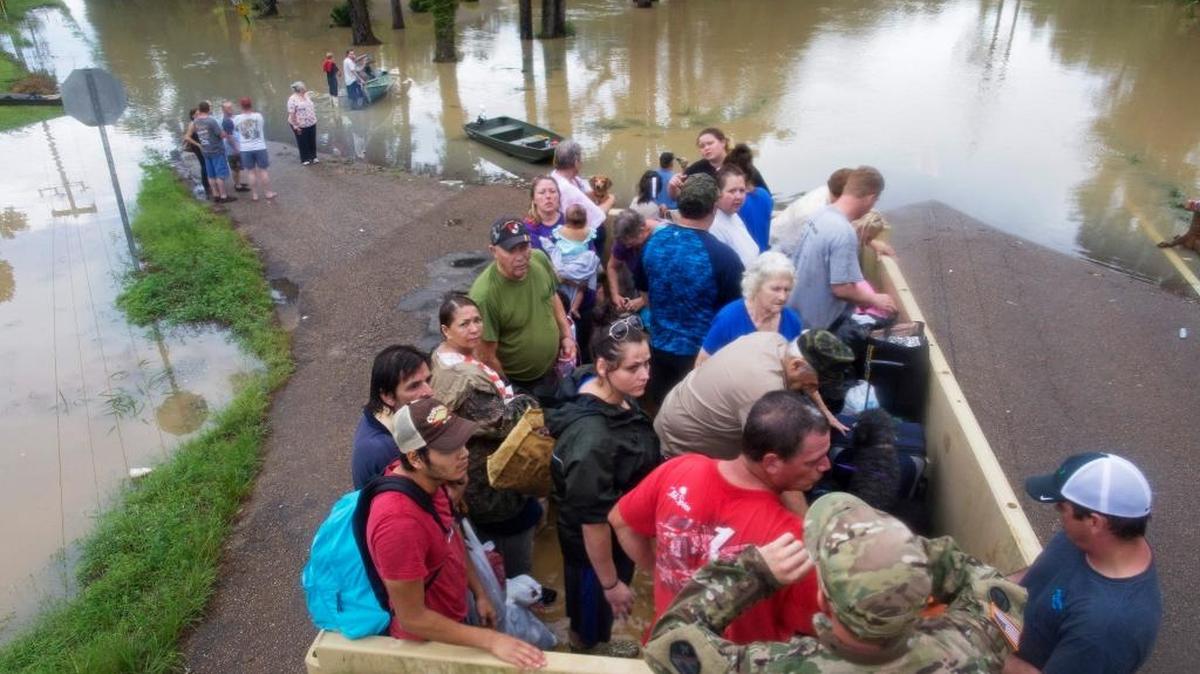 In this Aug. 14, 2016 file photo, Sgt. Brad Stone of the Louisiana Army National Guard gives safety instructions to people loaded on a dump truck after they were stranded by rising flood waters near Walker, La., after heavy rains inundating the region. The flooding killed at least 13 people, damaged 150,000 homes and cost at least $8.7 billion.