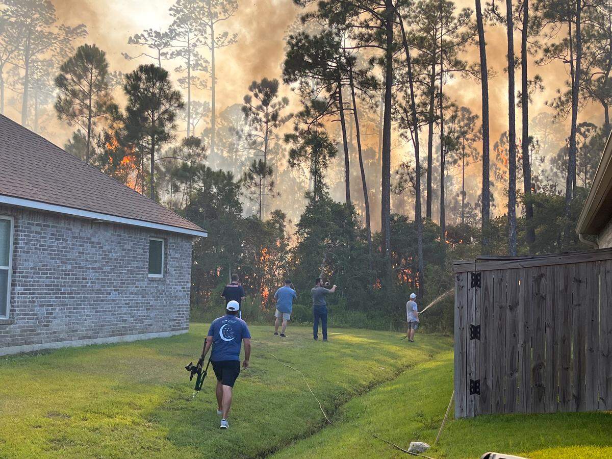 Talla Pointe residents use hoses and sprinklers as a woods fire spreads near the St. Martin subdivision on Thursday, Aug. 8, 2024.