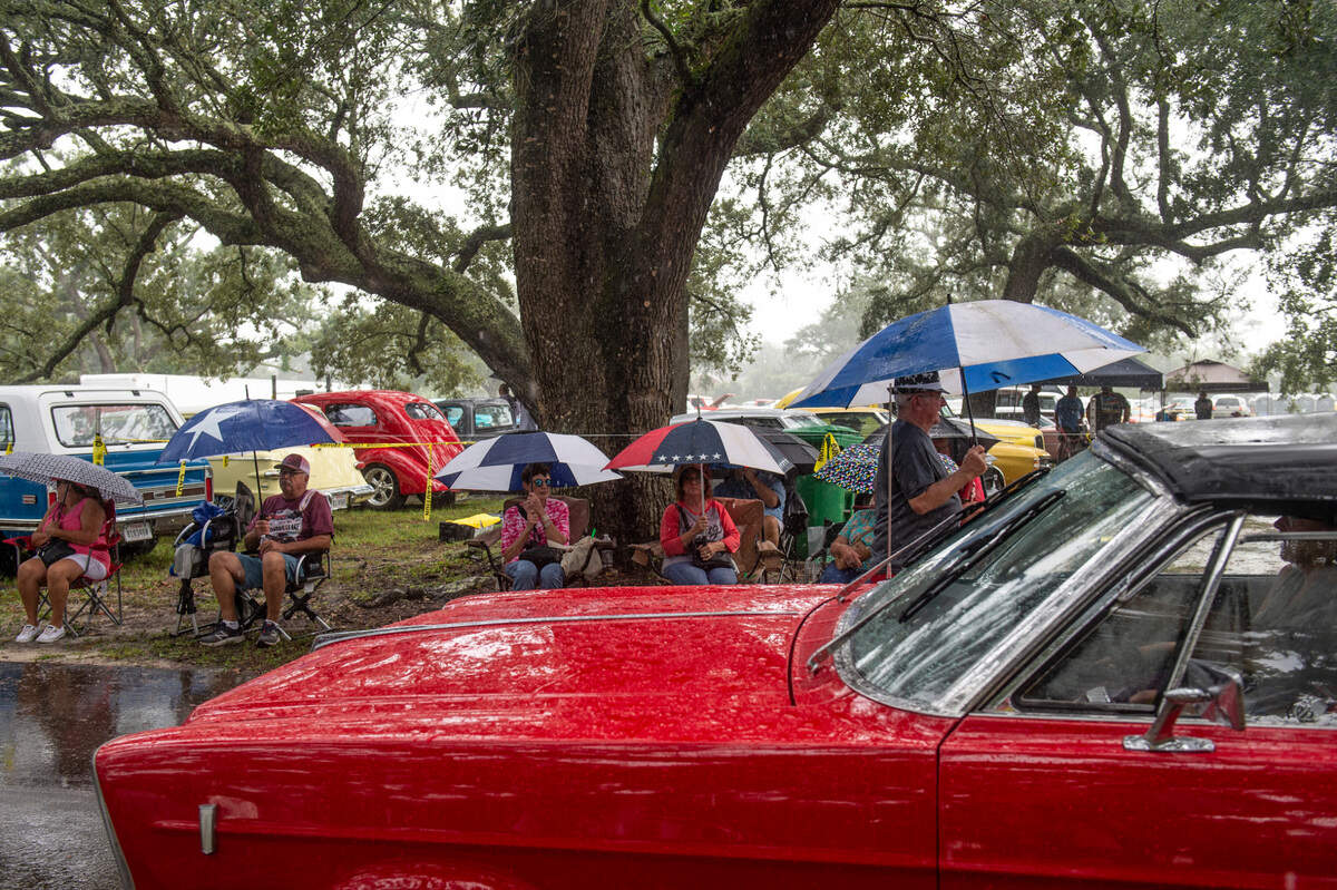 Onlookers with umbrellas watch cars pass by during Cruisin’ The Coast at Centennial Plaza in Gulfport on Monday, Oct. 4, 2021.